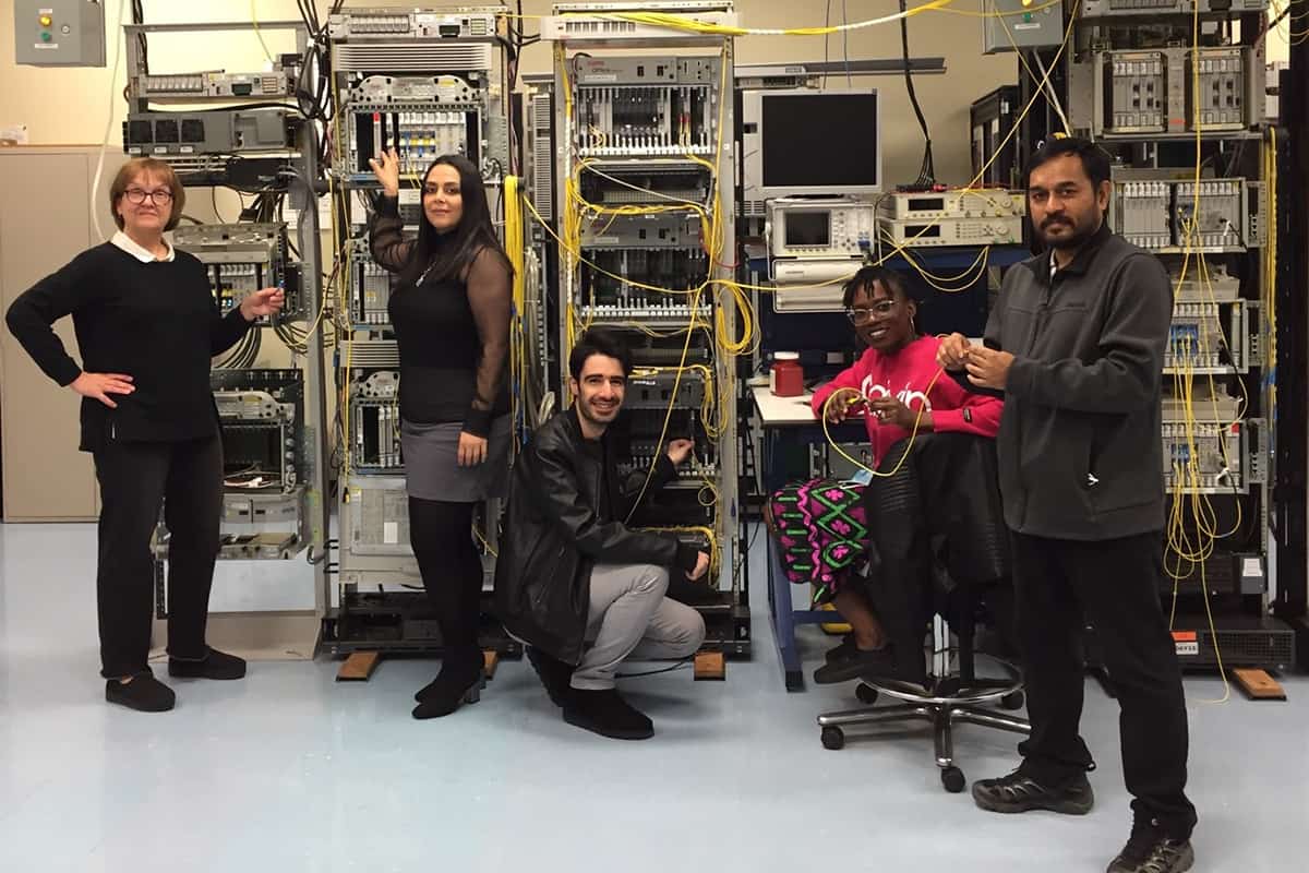 Five scientists sit and stand in front of telecoms equipment