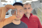Photo of Yongjie Wang holding a solar cell between his thumb and forefinger with Gerasimos Konstantatos in the background